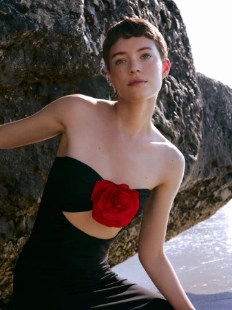 Model Loane Normand wearing a black strapless dress with a red rose accent against a rocky coast for Harper's Bazaar Greece.