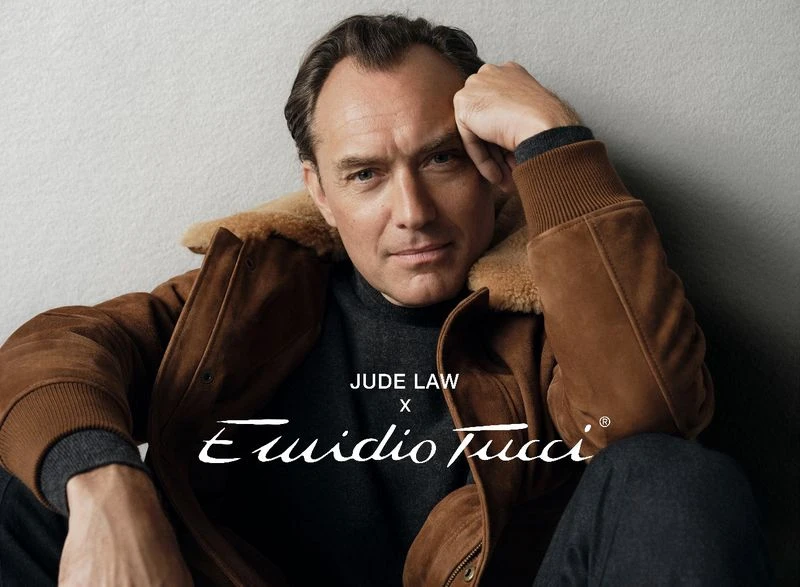 Jude Law wearing a brown shearling jacket and dark turtleneck sweater against a neutral textured background for an El Corte Ingles campaign.