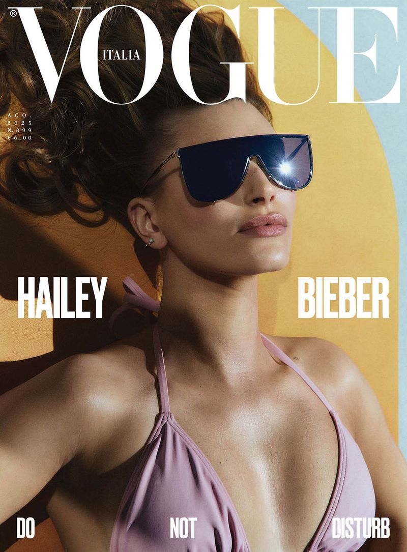 Vogue Italia cover features Hailey Bieber in lavender bikini top and oversized sunglasses, against a yellow and blue background.