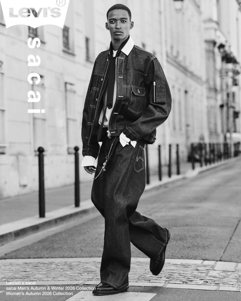Black and white editorial photo of a male model walking on a city street in a denim jacket and pants.