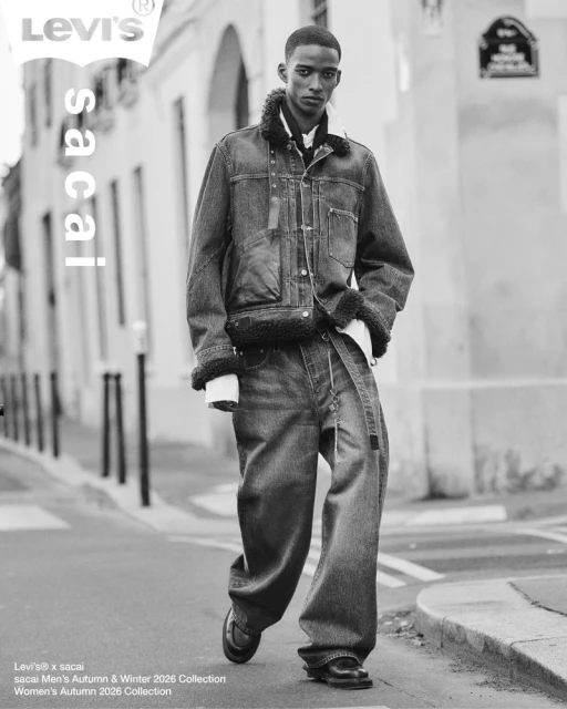 Black and white editorial photo of a young man walking down a city street wearing a layered denim jacket and loose jeans