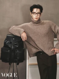 Man wearing black glasses and a brown turtleneck leaning on a black leather backpack for Vogue Hong Kong.