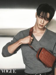 Man wearing a grey v-neck sweater with a brown cross-body bag against a textured background for Vogue Hong Kong.
