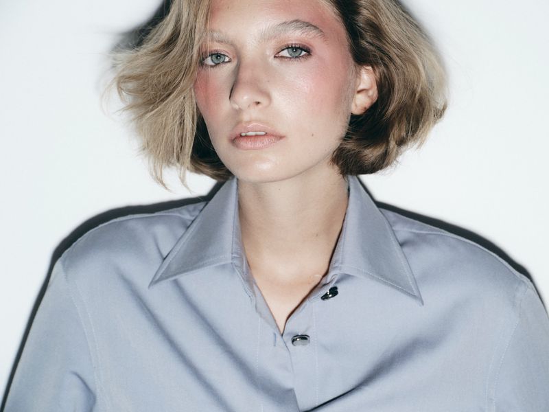 Model with blonde bob wearing a light blue button-up shirt against a plain white background for Harper's Bazaar Espana.