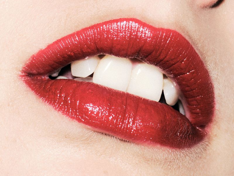 Close-up macro shot of glossy red lipstick on lips revealing white teeth for Harpers Bazaar Espana photographed by Javier Biosca.