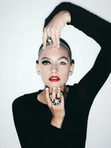Model in black top wearing statement rings with dramatic black and white eye makeup against a white background