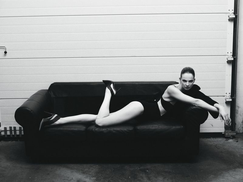 Model Eniko Mihalik lying on a black leather couch wearing a dark outfit for Forbes Spain, photographed by Javier Biosca.
