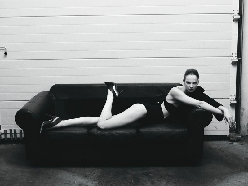Model Eniko Mihalik lying on a black leather couch wearing a dark outfit for Forbes Spain, photographed by Javier Biosca.