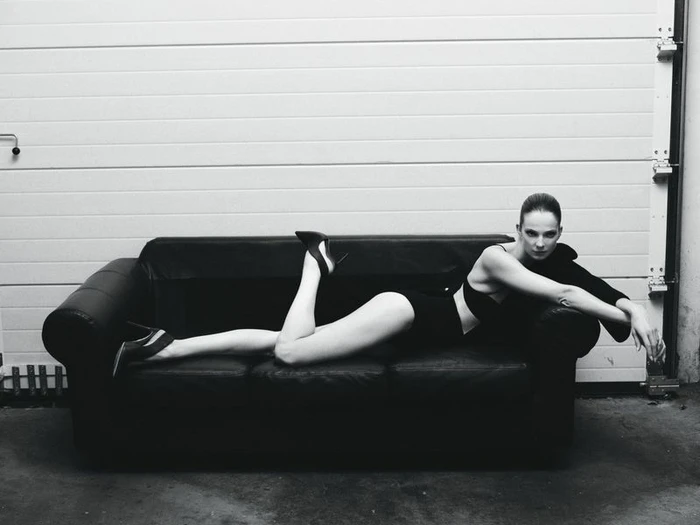 Model Eniko Mihalik lying on a black leather couch wearing a dark outfit for Forbes Spain, photographed by Javier Biosca.