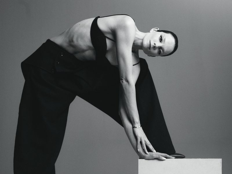 Model Eniko Mihalik posing in a black top and trousers against a neutral grey studio background for Forbes Spain.