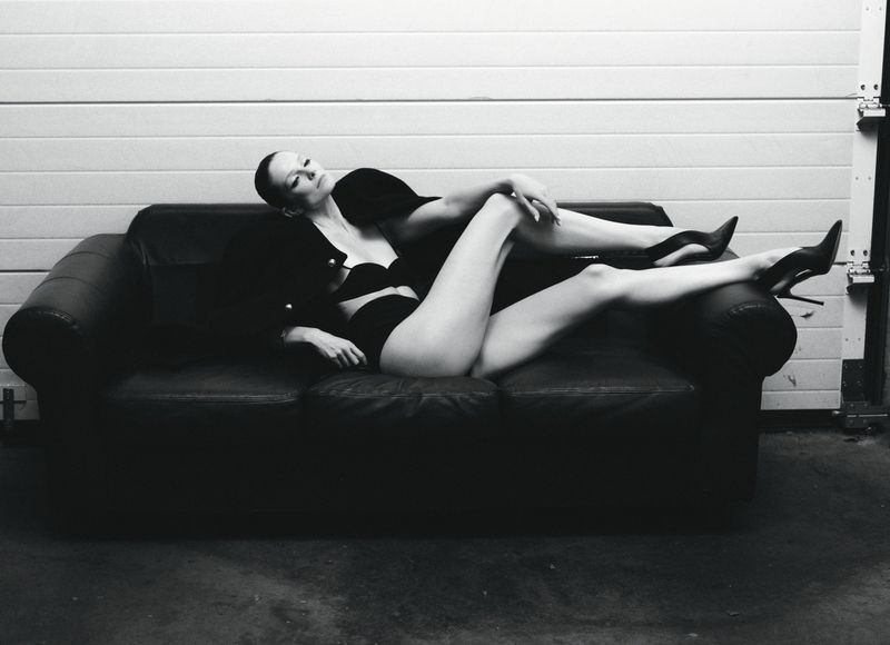 Eniko Mihalik reclining on a dark leather sofa in black lingerie and stilettos for Forbes Spain by Javier Biosca.