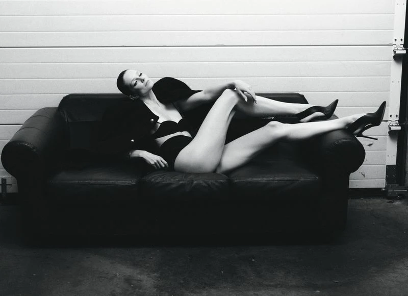 Eniko Mihalik reclining on a dark leather sofa in black lingerie and stilettos for Forbes Spain by Javier Biosca.