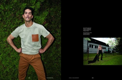 Man wearing pale green t-shirt with brown chest pocket and brown trousers posing against green foliage