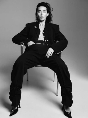Model wearing a black pantsuit seated in a metal chair against a grey studio background for Grazia UK editorial SUITS YOU