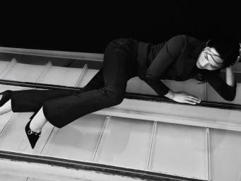 Model in black suit lying across a glass-paneled structure in a monochrome fashion shoot for Grazia UK