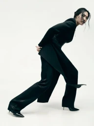 Model in black suit leaning forward against a white studio background