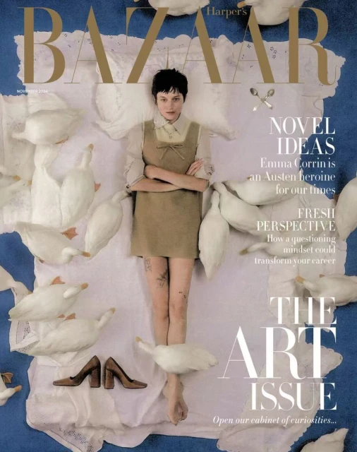 Emma Corrin lying on a quilted white blanket surrounded by white geese on a blue carpet for Harper's Bazaar UK November 2026 cover.