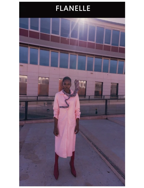 Model wearing a pink long shirt dress with a patterned scarf outdoors against a modern building exterior