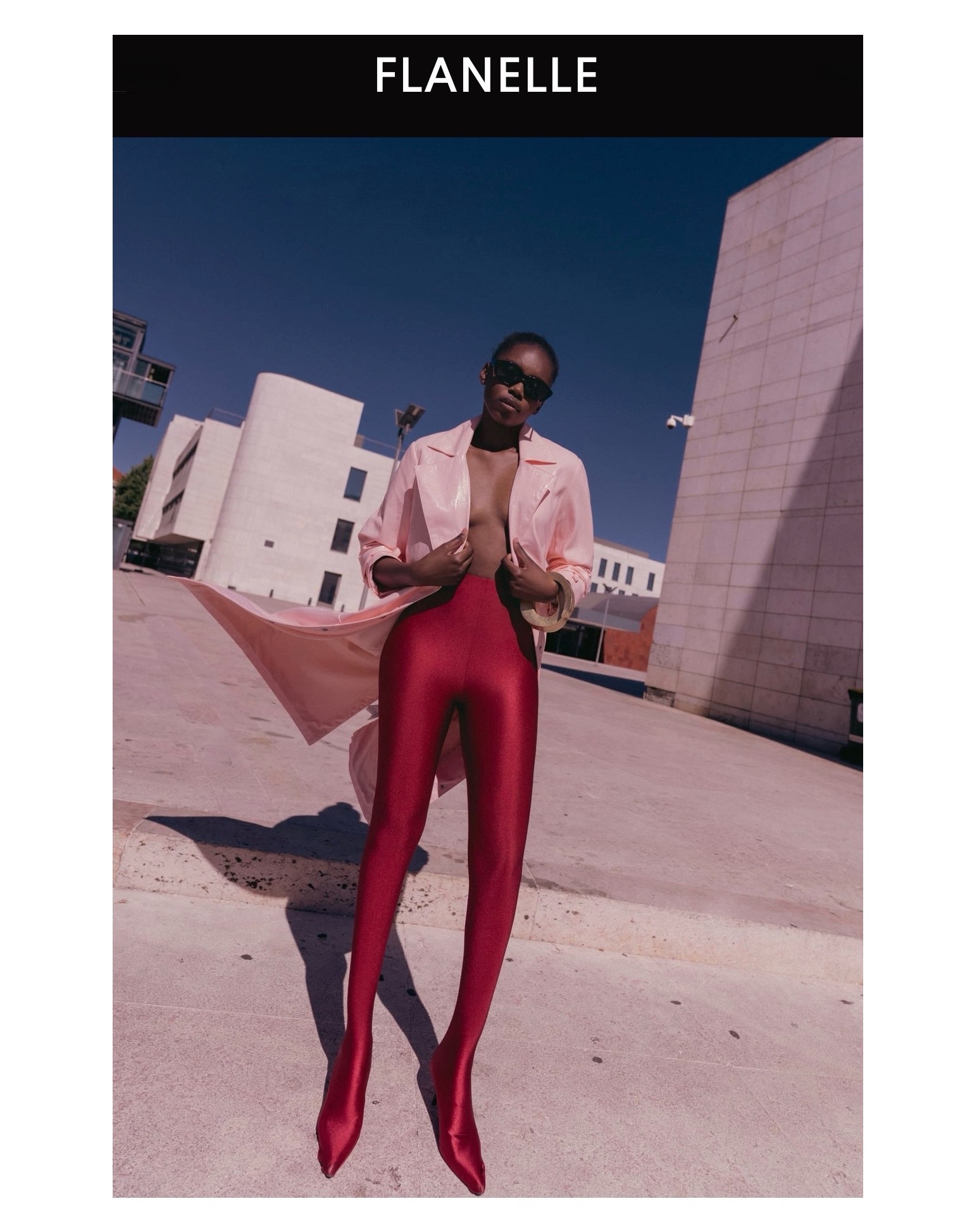 Model in shiny pink coat and glossy red tights standing outdoors against modern concrete architecture