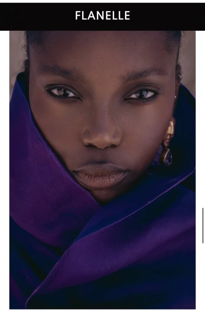 Close-up portrait of a Black woman wearing a deep purple high-collared coat and gold drop earrings for Flanelle Magazine.