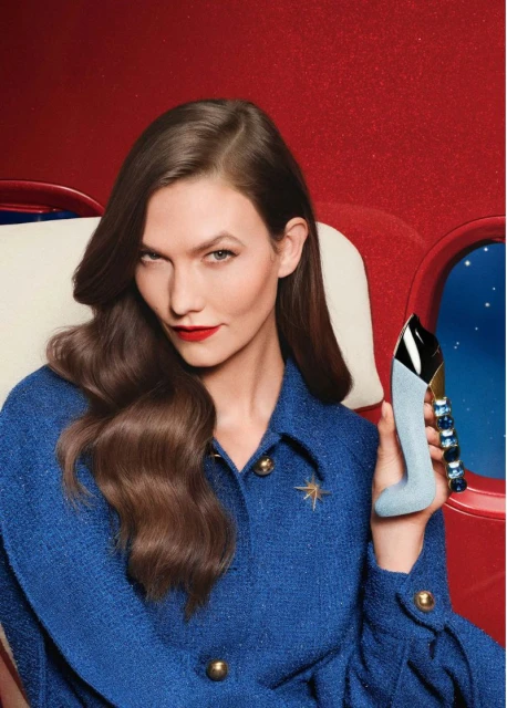 Model Karlie Kloss holding a shoe-shaped perfume bottle in a red and blue setting for Carolina Herrera