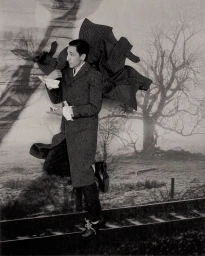 Adrien Brody wearing a patterned grey coat in front of a printed landscape backdrop with flying fabric