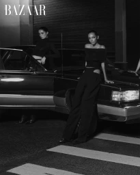 Two models in black outfits posing by a vintage car on a street at night for Harper's Bazaar Thailand