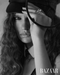 Monochrome portrait of a woman wearing a black leather cap and holding a magnifying glass near her face.