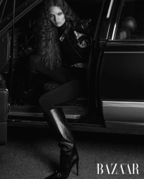Model with long curly hair wearing black leather jacket and tall boots sitting inside car