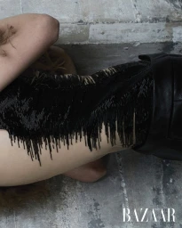 Model lying on textured stone floor wearing a black beaded fringe top and dark trousers for Harper's Bazaar Thailand