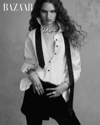 Model wearing a white collared shirt with a black scarf and statement jewelry for Harper's Bazaar