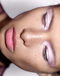 Extreme close-up portrait of a model with pink eyeshadow and glossy pink lips against a neutral background.