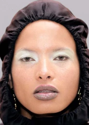 Close-up portrait of model Litza Veloz wearing a dark hooded garment and pale eye makeup for Puss Puss Magazine