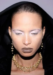 Close-up portrait of model Litza Veloz wearing gold statement jewelry and a black hooded garment for Puss Puss Magazine.