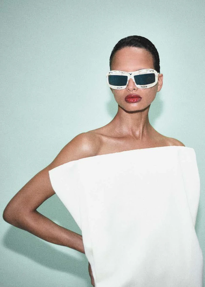 Model wearing white sunglasses and a structured white top against a pale mint background