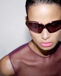 Close-up portrait of a model wearing dark tinted sunglasses and a purple top against a white background
