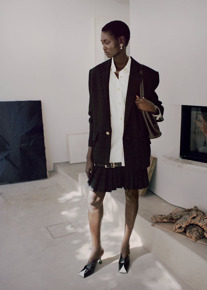 Model Ateta Jok wearing a black blazer and pleated skirt in Puss Puss Magazine editorial Silver Rain by Maya Skelton