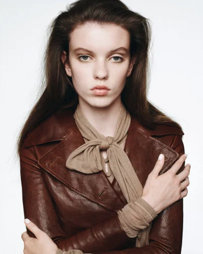 Model wearing a brown leather coat and tan scarf against a plain white background for Puss Puss Magazine