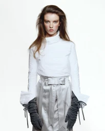 Model wearing a white turtleneck and grey bow skirt with long knitted gloves against a white seamless background