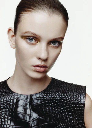 Close-up portrait of a model with slicked-back hair wearing a dark embossed leather top against a seamless white background.