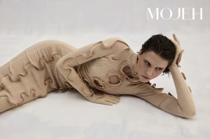 Model lying on a light background wearing a beige textured ribbed dress with cutout details and integrated gloves for Mojeh Magazine.
