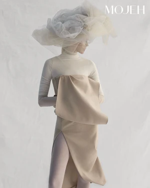 Model wearing a large sheer tulle hat and neutral sculptural garments against a white seamless background