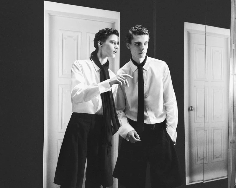 Two models in white shirts and black ties standing in an interior space with white doors in black and white.