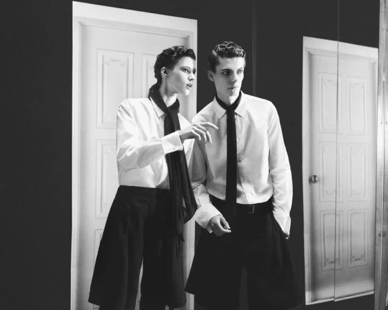 Two models in white shirts and black ties standing in an interior space with white doors in black and white.