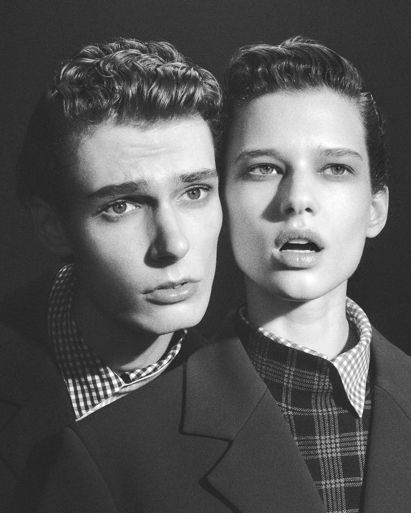 Black and white portrait of a male and female model wearing patterned shirts and dark blazers against a plain background.