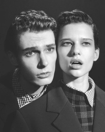 Black and white portrait of a male and female model wearing patterned shirts and dark blazers against a plain background.