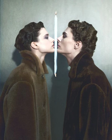 Two models in brown coats facing each other separated by a burning vertical candle