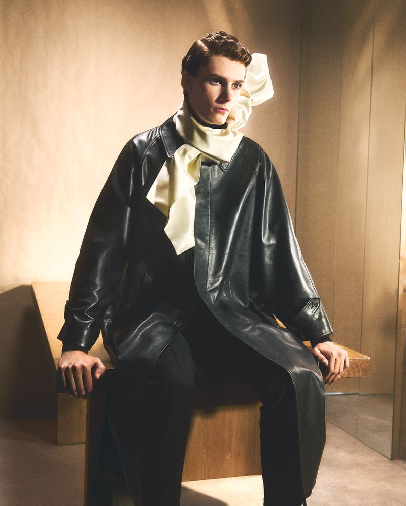 Model seated wearing a black leather coat and light yellow scarf for HTSI Magazine