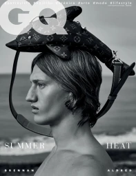 Black and white profile portrait of model Brennan Aldred balancing a dolphin-shaped monogram bag on his head against an ocean horizon.