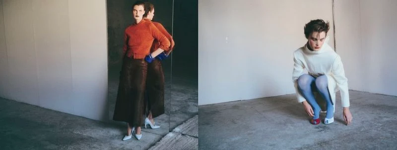 Model wearing orange top and dark skirt standing before a mirror in a minimal room for Vogue Greece